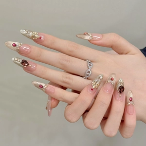 Detalle de uñas stiletto con pedrería roja y adornos florales dorados elegantes