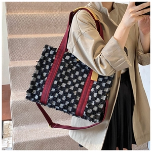 Detail of checkered denim tote bag with frayed edges and red adjustable shoulder strap