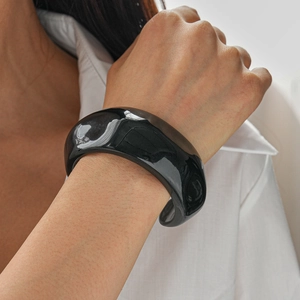 Close-up of a wide black resin cuff bracelet with polished finish on a woman's wrist