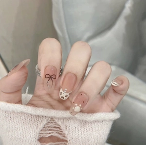 Press-on nails with leopard print, black bows, and nude matte finish on elegant hands
