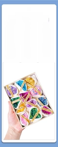 Close-up of 12 vibrant aura quartz geodes with golden labels in a white gift box