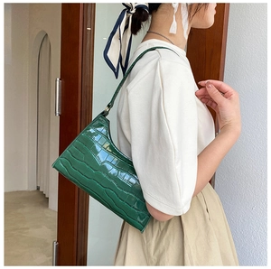 Detail showing deep green crocodile pattern baguette bag on model with textured finish