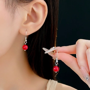 Gros plan de boucles d'oreilles ethniques en perles rouges portées et tenues à la main
