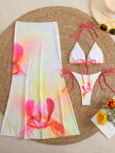 Flat lay of three-piece floral bikini set and mesh cover-up skirt on a woven mat