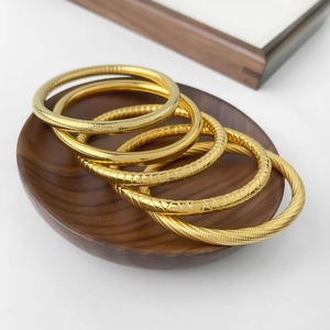 Set of five gold titanium steel bangles with textured patterns on a wooden tray