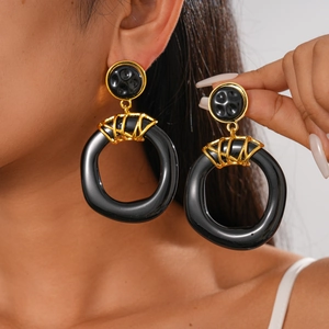 Close-up of black oversized resin hoops with gold metal accents worn by a model