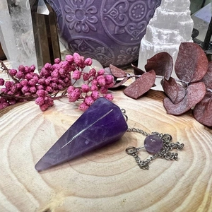 Polished hexagonal amethyst pendulum with silver chain on a natural wooden tray