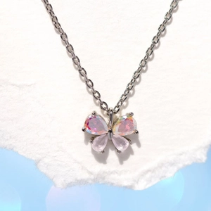 Macro shot of silver butterfly pendant featuring pink iridescent crystals on white paper