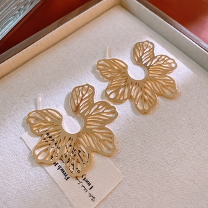 Macro shot of gold hollow flower earrings on beige velvet lining with soft lighting