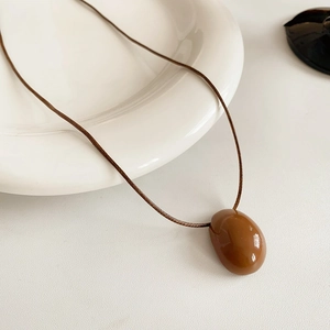 Détail du pendentif ovale caramel brillant sur un cordon minimaliste de couleur brune