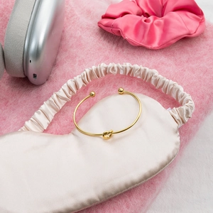Detail of 18K gold knot bracelet with spherical ends on champagne silk fabric background