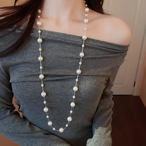 Detailed view of elegant long necklace with white pearls on silver chain over grey sweater