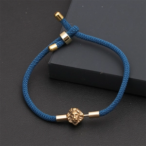 Detailed view of blue woven rope bracelet with gold lion head charm on black leather texture
