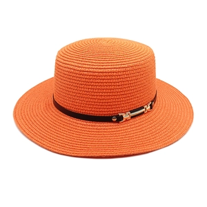 Détail d'un chapeau de paille orange avec ruban en cuir noir et boucle mors dorée élégante