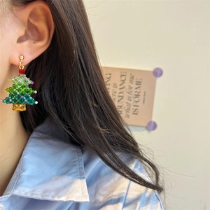 Detail of handmade beaded Christmas tree earrings with colorful crystals on a model
