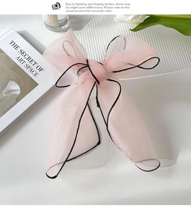 Detailed view of light pink organza bow hair tie with elegant black stitched edges