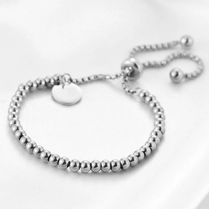 Detail view of adjustable silver beaded bracelet with round tag on white satin