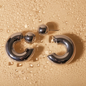 Macro shot of silver C-shaped steel earrings with sphere back on water droplet surface