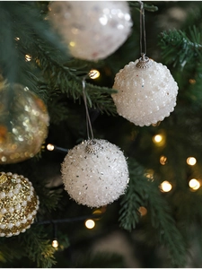 Detailed view of white embossed and silver sequined Christmas balls on a glowing tree
