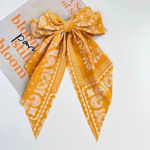 Detail of yellow paisley chiffon hair bow clip with long ribbons on a stylish background