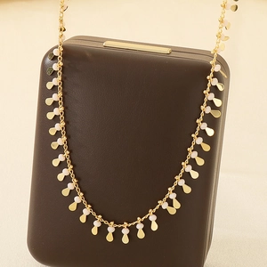 Detail view of gold necklace with delicate white teardrop pendants on jewelry box