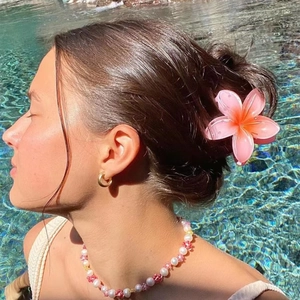 Pink Y2K plumeria flower hair claw clip worn by a model at a sunny poolside beach setting