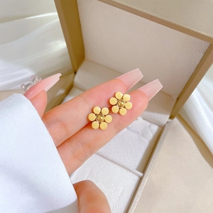 Pendientes minimalistas de flores de seis pétalos en oro mate sostenidos a mano