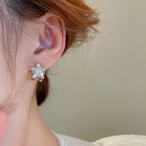 Detail of silver star-shaped earring with pavé zircon stones on a model's ear