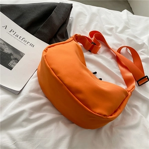 Minimalist bright orange nylon half-moon crossbody bag with wide shoulder strap on white sheets