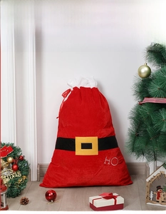 Detail of red velvet Santa gift bag with HO HO HO embroidery and belt design in festive setting