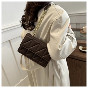 Close-up of dark brown quilted crossbody bag with gold chain strap on beige coat