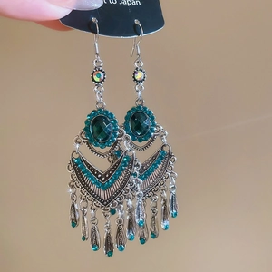 Detail of silver fish-shaped ethnic earrings with green gems and dangling tassels