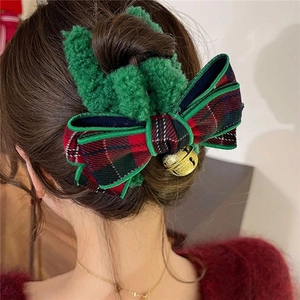Close-up of green plush hair claw clip with red-green plaid bow and golden bell detail