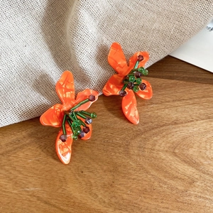 Detail view of orange floral earrings with stone bead centers on a rustic wood surface