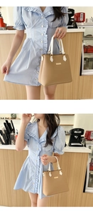 Close-up of khaki PU leather handbag with gold hardware and white handles shown by model