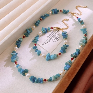 Flat lay of aquamarine beads and white pearls necklace with red accents and gold clasp