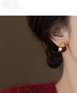 Close-up of gold gourd earrings with red beads and heart charms worn by a model