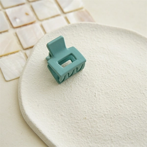 Close-up of a matte teal square hair claw clip on a textured ceramic dish