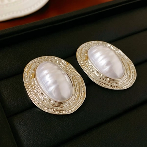 Close-up of vintage oval metal stud earrings with textured gold frame and faux pearl inlay