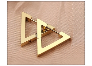 Close-up of geometric triangle gold hoop earrings on soft pink satin fabric background