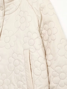 Detailed view of cream quilted floral pattern and hidden pocket on women's winter jacket