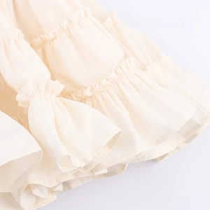 Détail de la texture plissée crème multicouche et de l'ourlet à volants de la robe