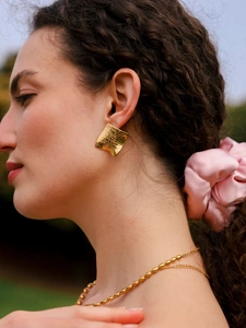 Macro shot of gold square earrings with wavy texture and beaded chain necklace detail