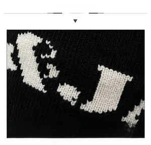 Close-up of thick black knit beanie showing detailed white letter jacquard texture