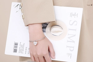 Gros plan d'un bracelet cœur en argent avec gravure MOM au poignet d'un mannequin