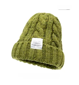 Detailed view of chunky grass green cable knit beanie with white square woven label