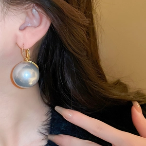 Gros plan d'une boucle d'oreille en perle gris argenté avec crochet doré sur l'oreille