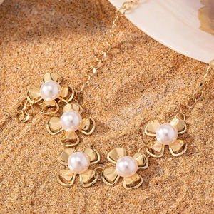 Elegant gold necklace with floral pendants and pearls on a sandy beach background