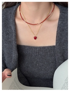 Close-up of layered red beaded necklace and gold heart pendant on a model with a knit sweater
