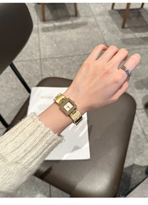 Gros plan d'une élégante montre carrée dorée avec cadran ivoire au poignet dans un café